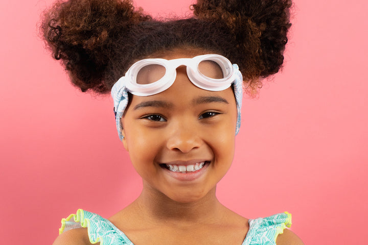 Enfant portant des lunettes de piscine blanches avec maillot de bain sur fond rose.