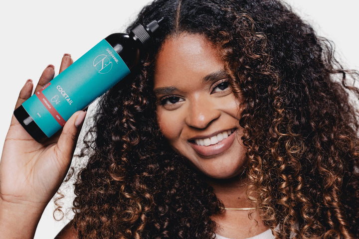 Femme aux cheveux bouclés tenant un soin capillaire Skweli Hair pour hydrater les cheveux texturés.