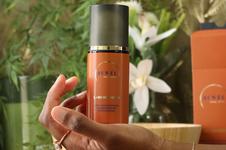 Flacon OUWEL Lash Shampoo – nettoyant pour extensions de cils tenu en main dans un décor naturel.