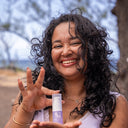 Femme aux cheveux bouclés montrant un sérum capillaire Musc Soyeux pour cheveux texturés.