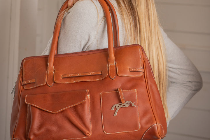 Sac à main en cuir marron porté à l’épaule par une femme, modèle élégant avec grandes poignées.